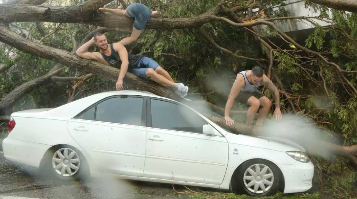 Tourists pose for selfies on top of a damaged car after Tropical Cyclone Marcus hit Darwin's CBD. Photo: AAP

