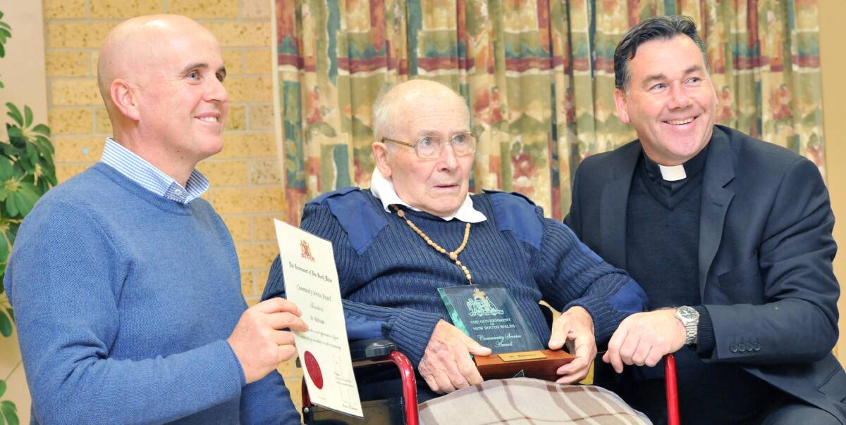 TIRELESS: Adrian Piccoli and Father Andrew Grace kneel next to Father Rafe Beltrame after he recieved his community service award. Picture: Anthony Stipo.