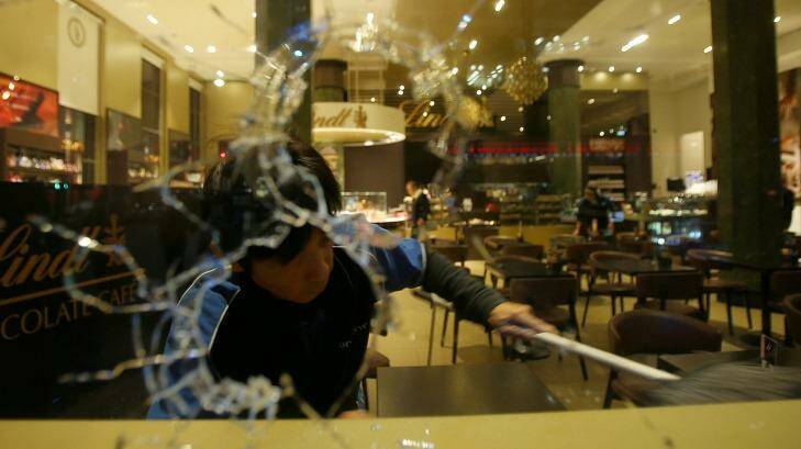 A man cleans up broken glass from vandalised windows at the Lindt cafe in Martin Place, Sydney. Photo: Kate Geraghty
