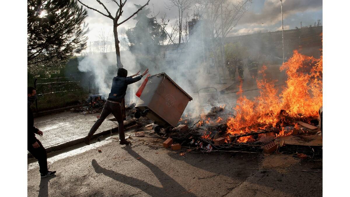 A protester throws a garbage bin into a burning barricade during a protest against the government's education reforms and cutbacks in university grants and staffing in Campus Ciudad Universitaria on March 26, 2014 in Madrid, Spain. Photo: Getty Images.