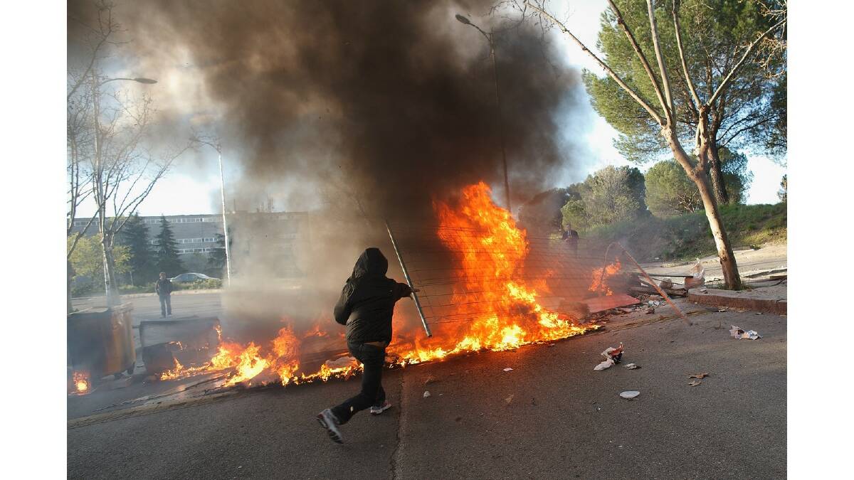 A protester throws a fence into a burning barricade during a protest against the government's education reforms and cutbacks in university grants and staffing in Campus Ciudad Universitaria on March 26, 2014 in Madrid, Spain. Photo: Getty Images.