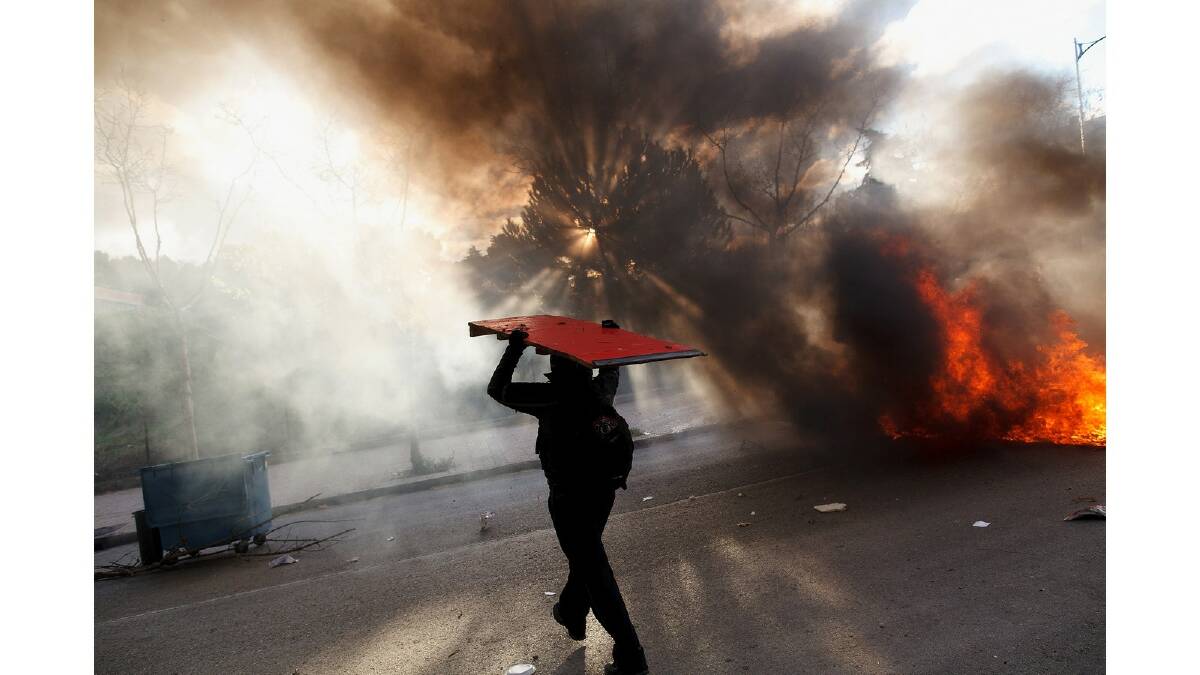A protester carries a wooden table as he walks next to a burning barricade during a protest against the government's education reforms and cutbacks in university grants and staffing in Campus Ciudad Universitaria on March 26, 2014 in Madrid, Spain. Photo: Getty Images.
