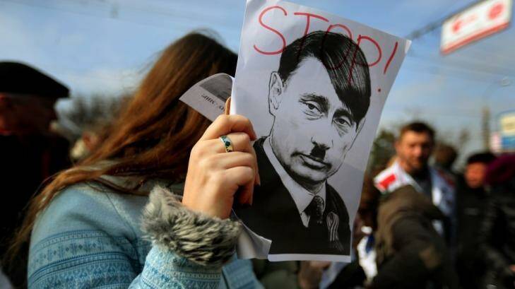 A woman covers her face with a poster of Russian President Vladimir Putin with facial features resembling Adolf Hitler, at Shevchenko Park during a Pro-Ukrainian rally, in Simferopol, Crimea. Photo: Kate Geraghty