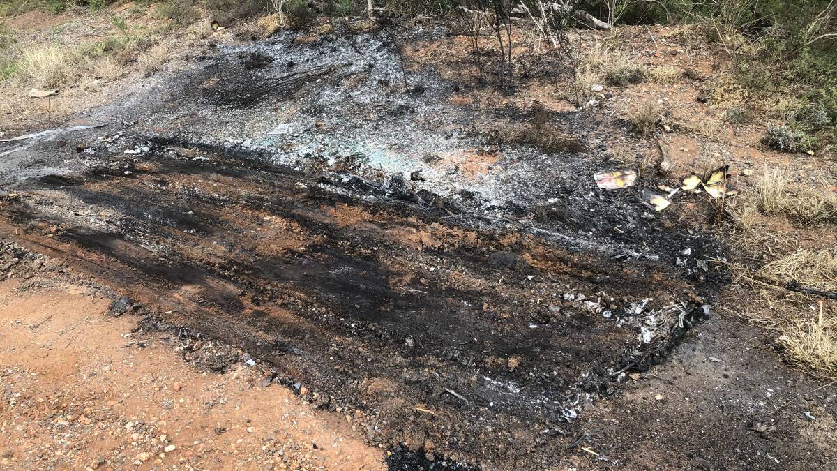 BROKEN GLASS: Charcoal, tire tracks and broken glass is all that currently remains of the burnt-out car on Beelbangera Road. PHOTO: Cai Holroyd