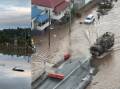A flooded street will still water and floating debris in Lismore on Thursday (left) and an ADF vehicle that made its way through floodwaters on Wednesday (right). Left photo: @scottybrizzle. Right photo: Angus Gray.