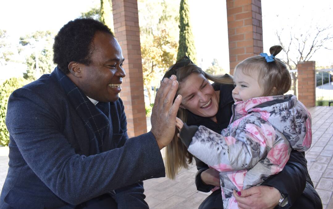 GIMME FIVE: Father Christian Obiekwe high fives one of his littlest congregants Elizabeth Johns and her mum Nadine Johns. Father Obiekwe will give one last mass session on July 21. PHOTO: Kenji Sato