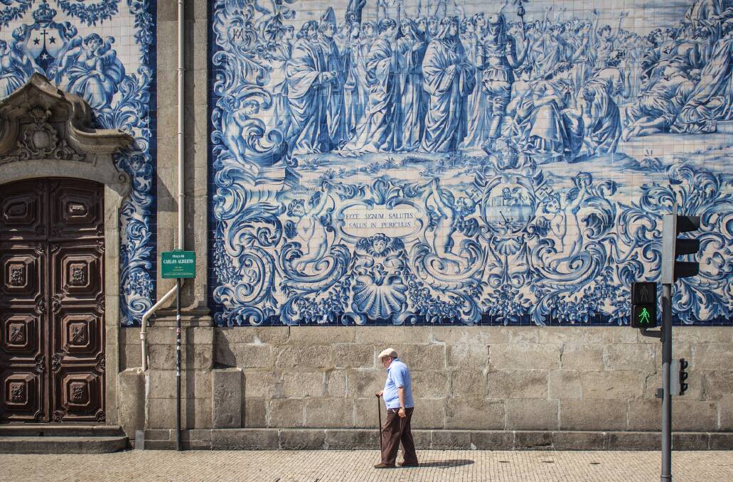 A man walks in front of some of the iconic blue tile art that covers many of the walls in Porto, Portugal.
