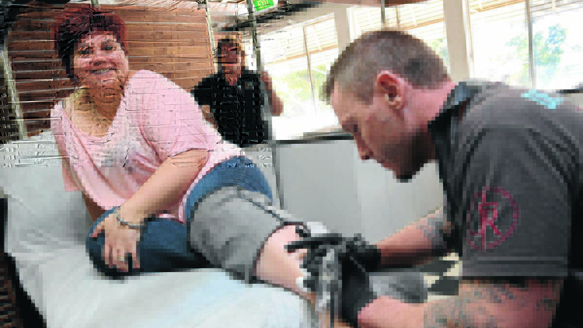 GRIN AND BEAR IT: Aimee Gibbs gets inked for autism with tattoo artist Bo Smith, while organiser Nicole Horley looks on. 